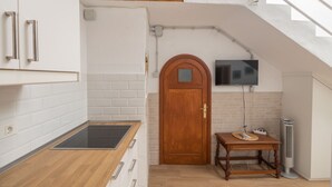 Una cocina compacta con armarios blancos, encimera de madera, estufa integrada, puerta de madera, una pequeña mesa con felpudo y un televisor montado en la pared.