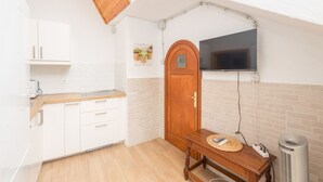 Una cocina compacta con armarios blancos, una puerta de madera, un televisor montado en la pared y una mesita con un tapete.