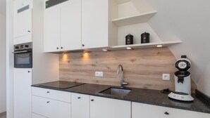 Een moderne keuken met witte kasten, een dubbele spoelbak, een inbouwoven en een koffieapparaat.