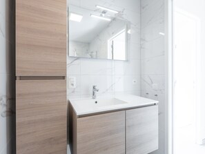 A modern bathroom with a white sink, wooden cabinetry, and a large mirror. - Vakantiestraat 4 Coastal Nest (Middelkerke)