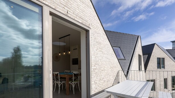 Een modern huis met een eethoek, een groot raam en een houten terras.