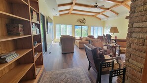 A spacious living room with a high ceiling, wooden beams, and a stone accent wall. There are multiple seating areas with sofas and chairs, and a large window providing natural light. - Bluestone Manor--spacious mountain home for your next adventure (Nimitz)