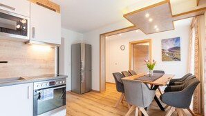 Eine moderne Küche mit Einbauofen, Kühlschrank und Essbereich mit Holztisch und grauen Stühlen.