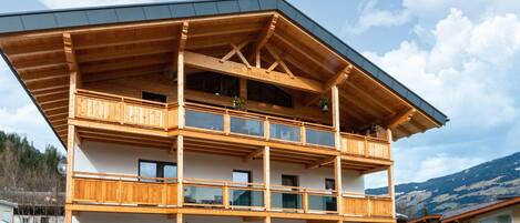 A multi-story wooden building with balconies, large windows, and a stone facade.