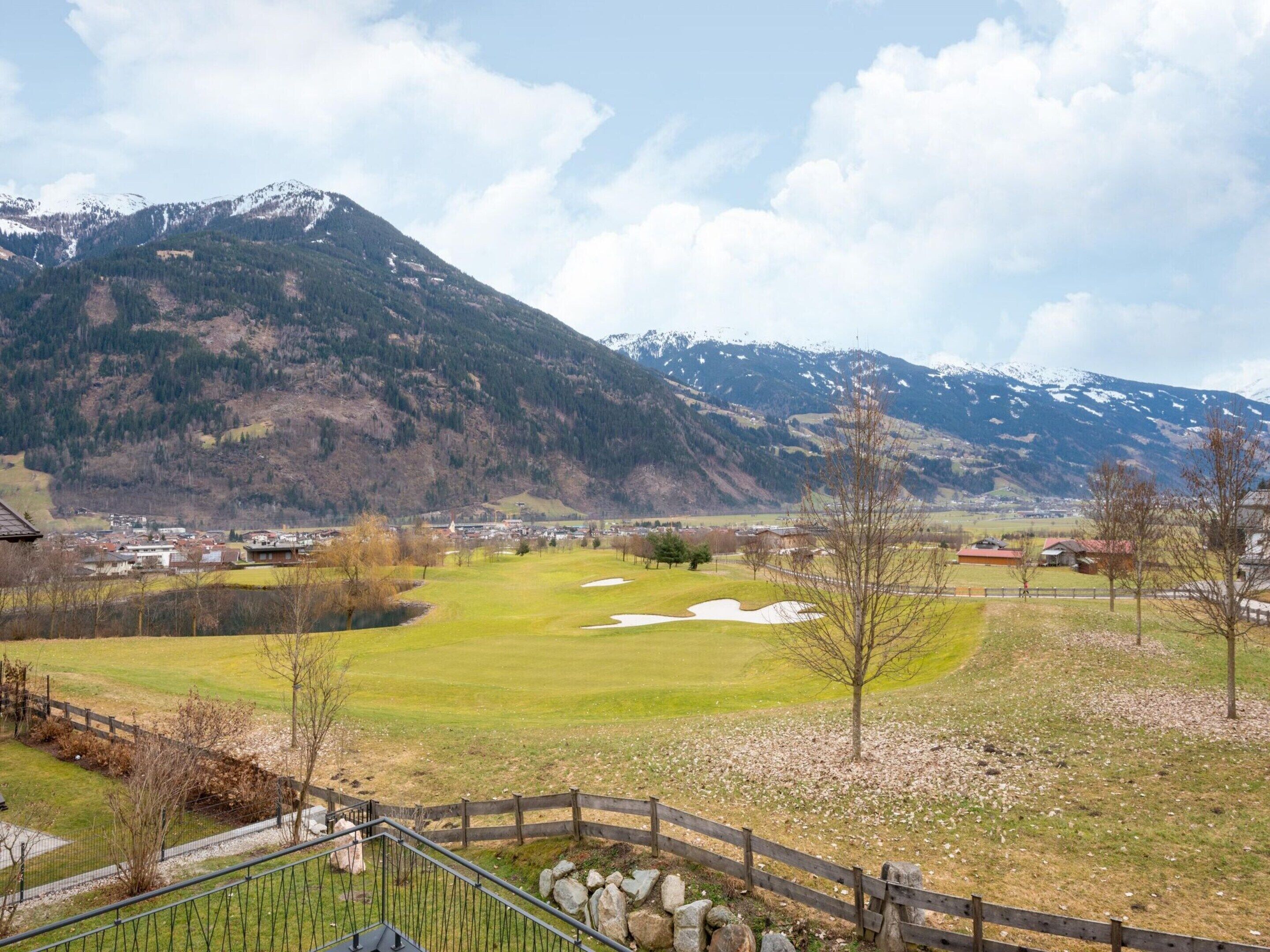 Un paisaje montañoso con un pueblo en el valle, un campo de golf y una valla de madera.