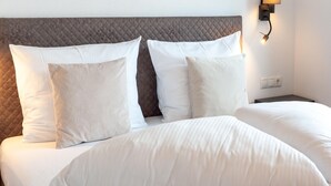 Ein ordentlich bezogenes Bett mit weißer Bettwäsche und Kissen, ein gestepptes Kopfteil und eine an der Wand befestigte Leuchte.