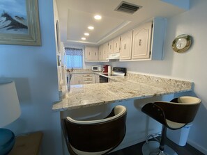 A kitchen with a marble countertop, white cabinets, a microwave, and a clock on the wall.
