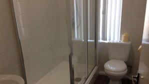 Un baño con ducha envuelta en vidrio, inodoro y lavamanos.