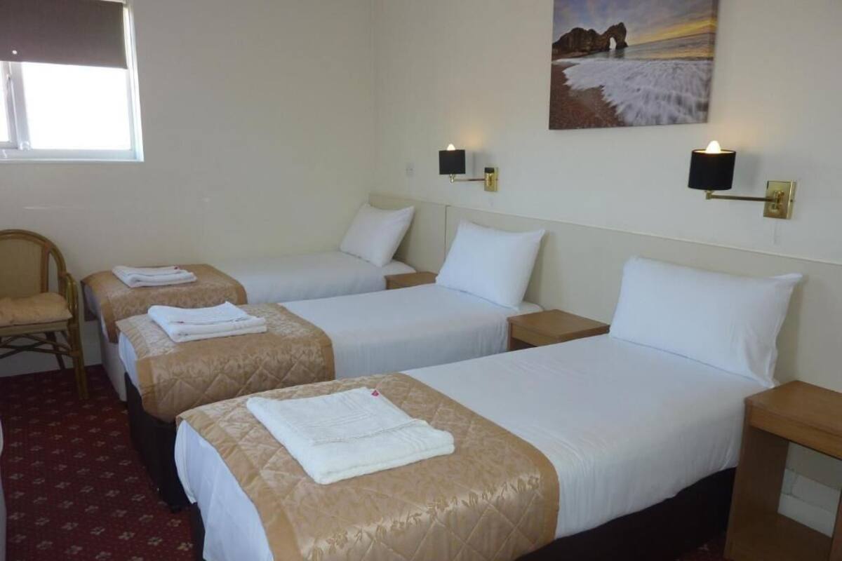 A hotel room with three single beds, a chair, and a painting on the wall.