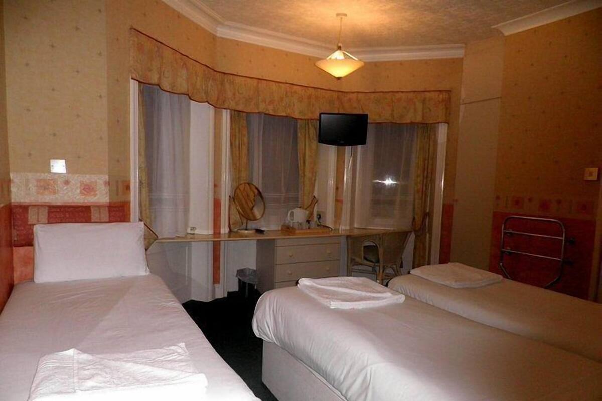 A hotel room with two single beds, a desk with a mirror, a television, and a window with curtains.