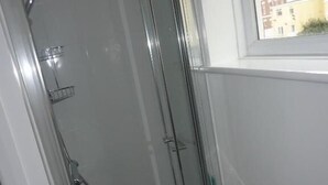 Un baño con ducha de vidrio, lavamanos y ventana con vistas a edificios.