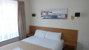 Habitación de hotel con una cama grande, un cuadro en la pared, una ventana con cortinas y una mesita de noche.