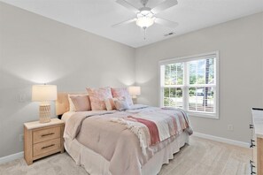 A bedroom with a bed, nightstands, a ceiling fan, and a window with blinds.