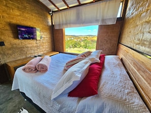 Una cama bien hecha con almohadas blancas y rojas, una toalla enrollada y un cabecero de madera.