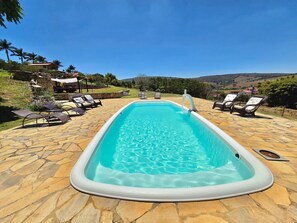 Una piscina rectangular con solárium de piedra, rodeada de sillones de descanso y un muro de piedra.