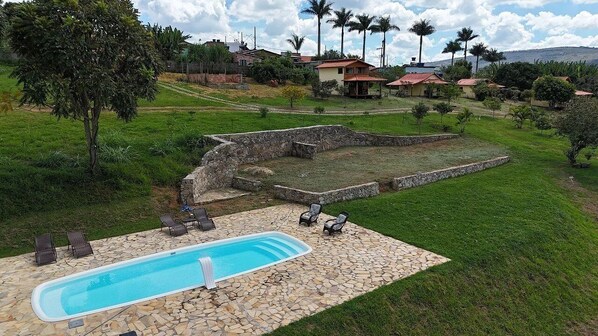 Una piscina con baldosas de piedra, rodeada de césped y un muro de piedra.