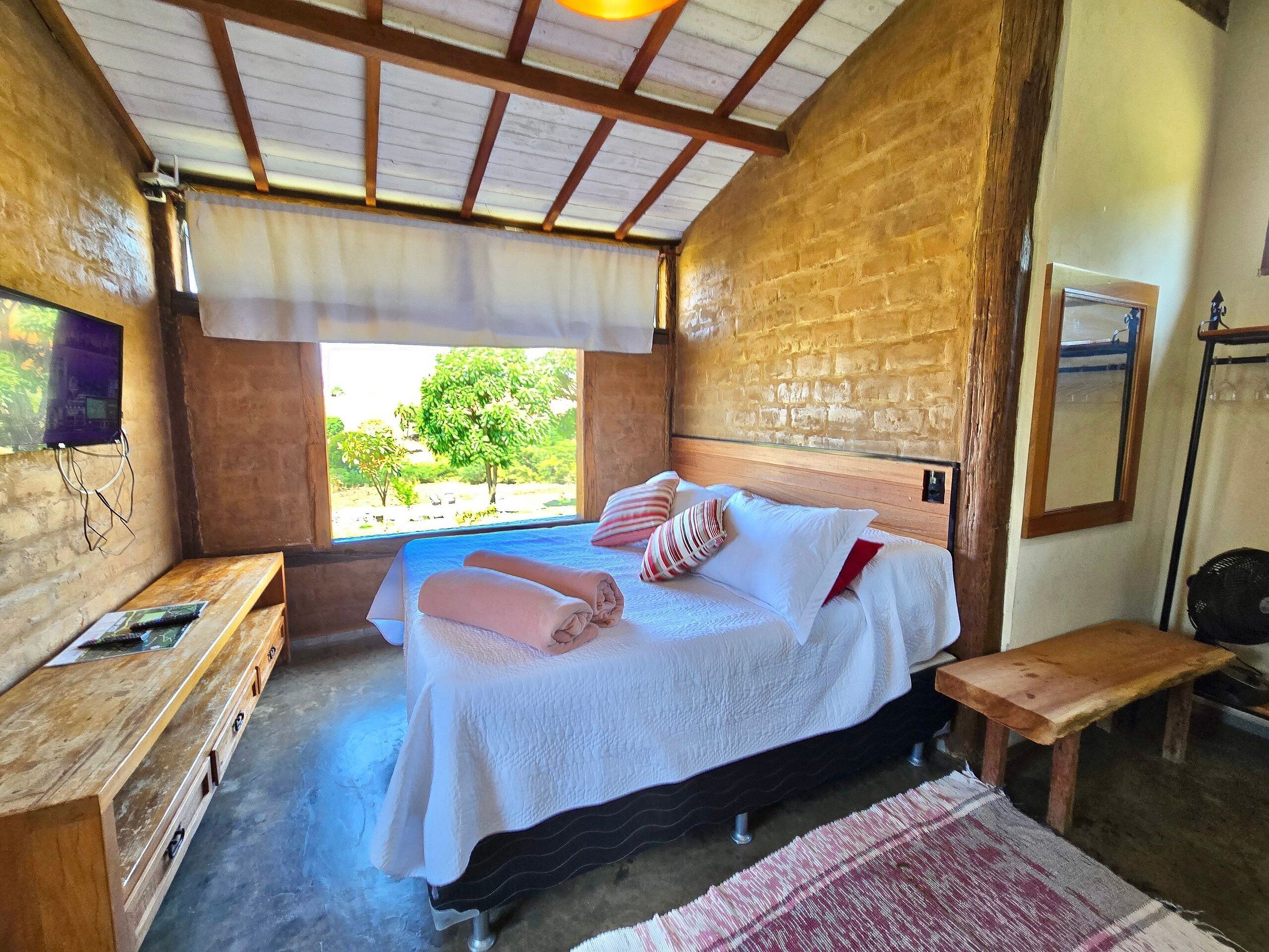 Un dormitorio con cama, mesitas de noche, una ventana con vistas y una pared de ladrillo.