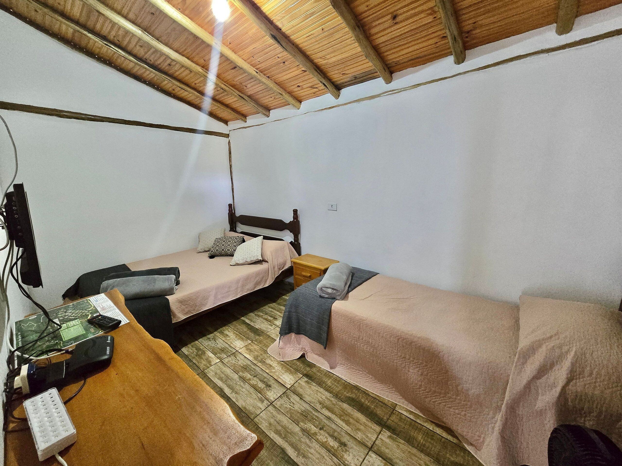 Una habitación pequeña y sencilla con dos camas individuales, un escritorio de madera y un sistema eléctrico básico.