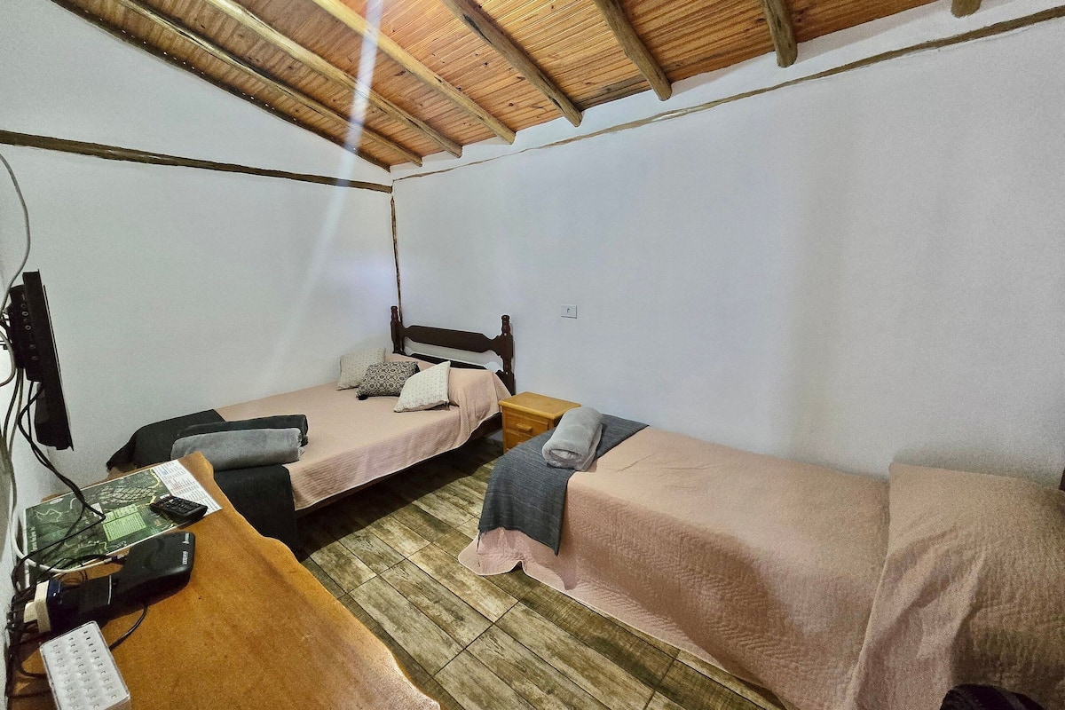 Una habitación pequeña y sencilla con dos camas individuales, un escritorio de madera y un sistema eléctrico básico.