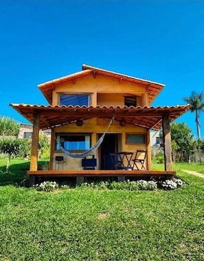 Una casa de dos pisos con un porche de madera, una hamaca y mobiliario exterior.