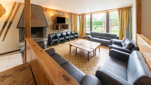 A modern living room with a stone fireplace, leather sofas, and a television mounted on the wall. - Villa in Ardennes With Sauna and Jacuzzi (Durbuy)