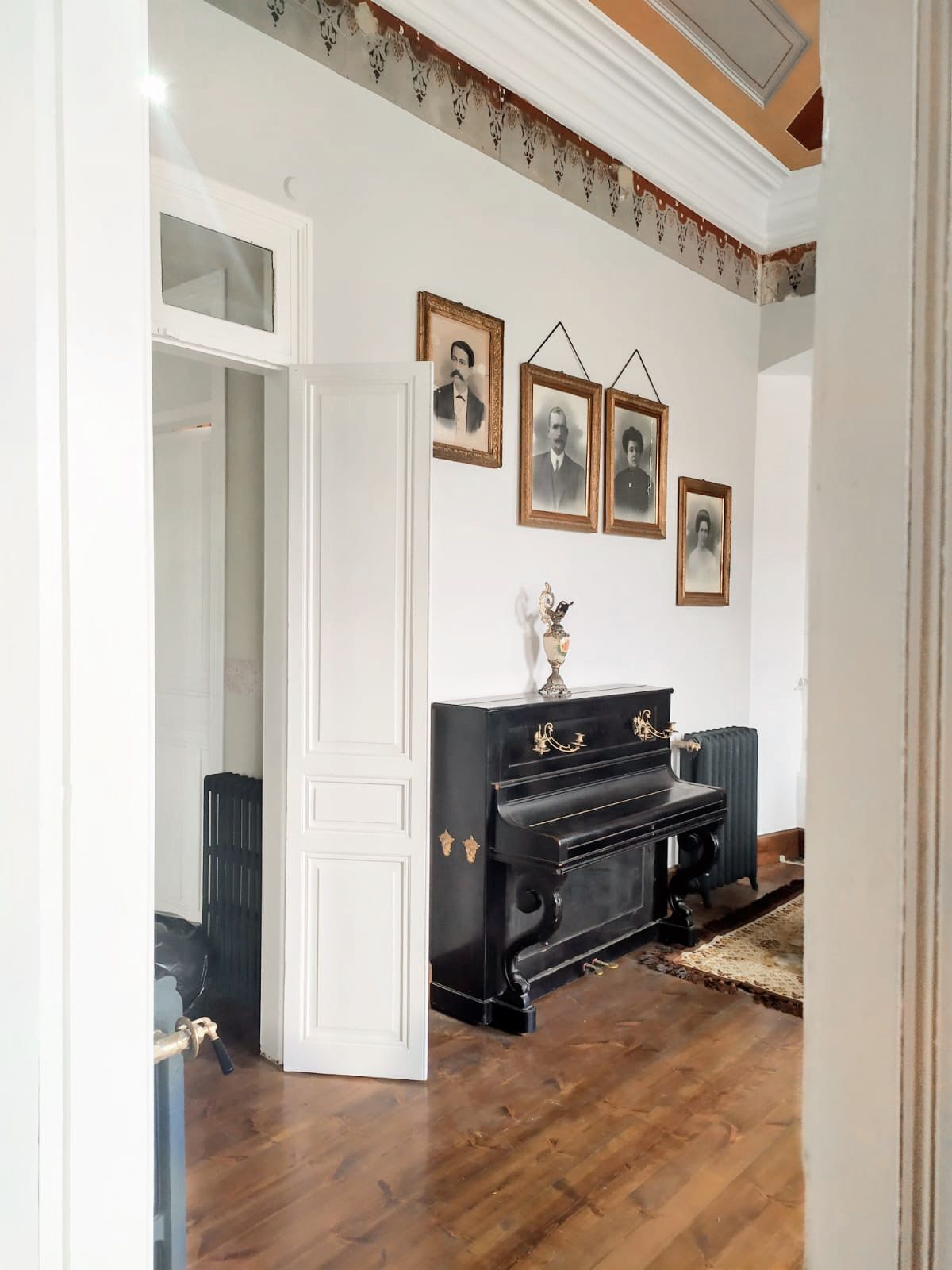 Una habitación con un piano negro, un radiador y una puerta que da a otra estancia.
