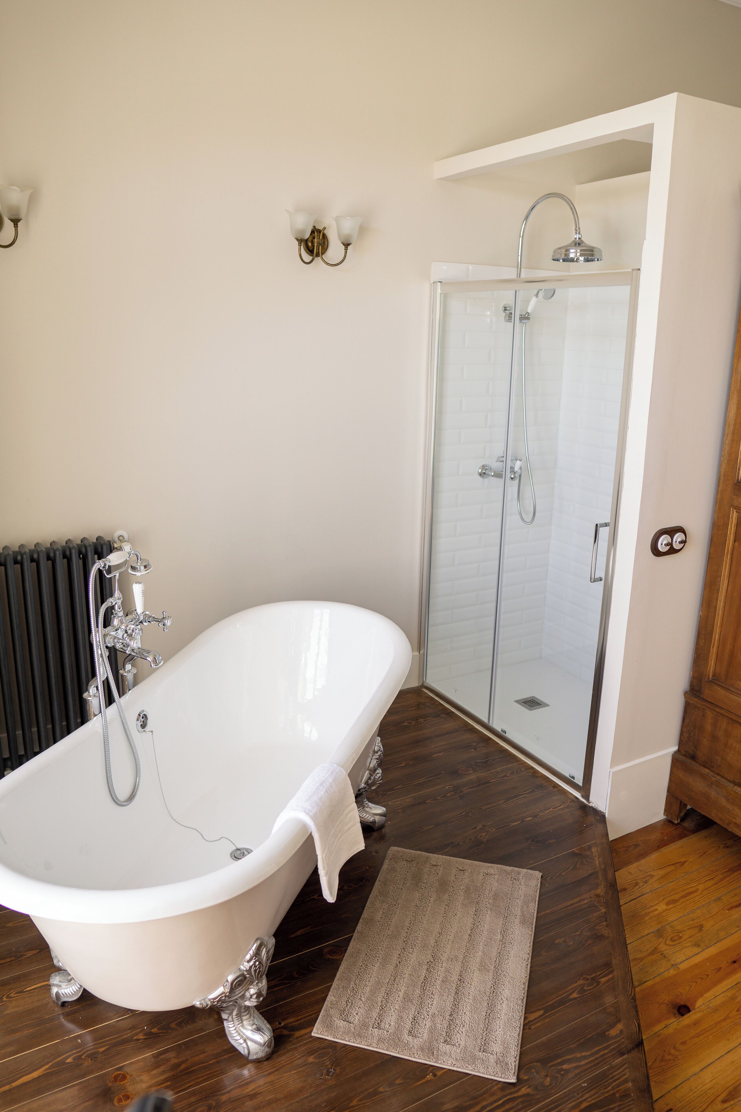 A bathroom with a freestanding bathtub, a glass-enclosed shower, and a wooden floor.