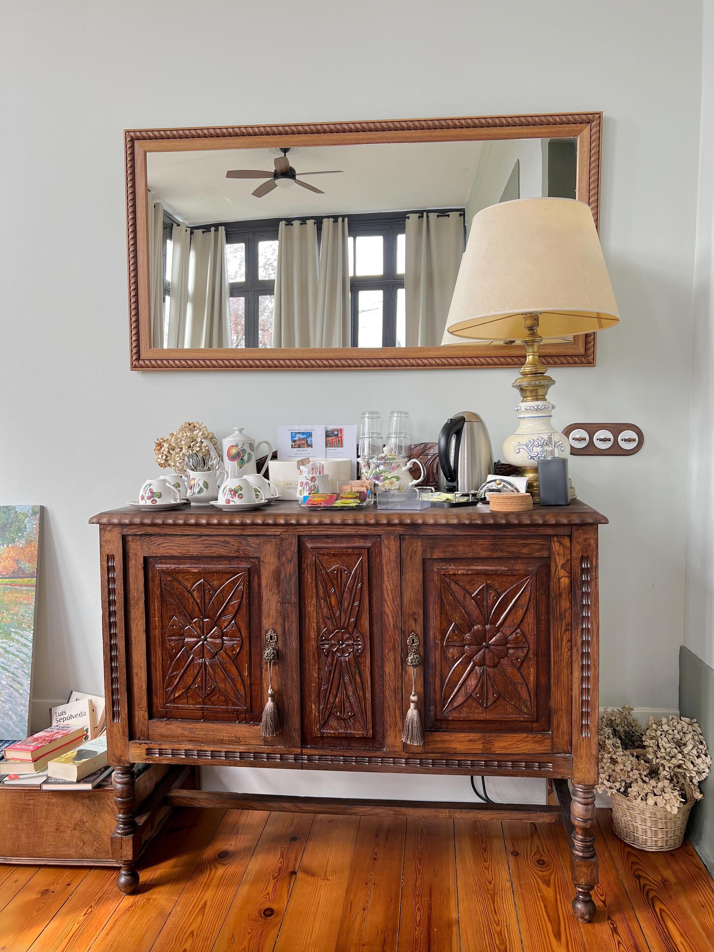 Een houten kast met decoratieve houtsnijwerken, een spiegel erboven en een lamp op de bovenkant.