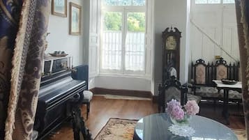 Ein Zimmer mit einem Klavier, einem runden Tisch mit Blumenvase und einer Kristallleuchter.