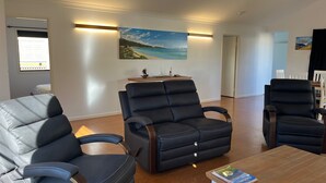 Ein modernes Wohnzimmer mit zwei schwarzen Ledersesseln, einem Holztisch und einem Gemälde mit Strandmotiv an der Wand.