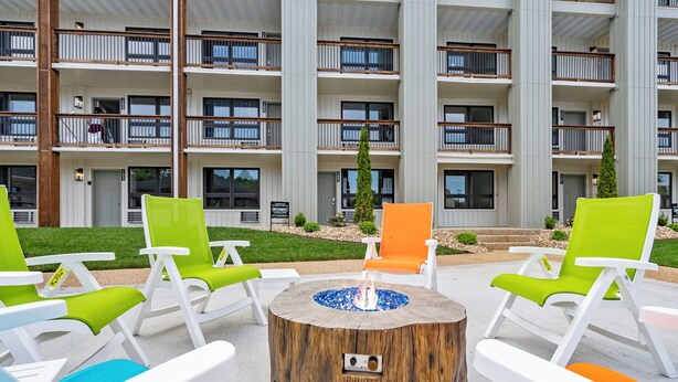 A modern outdoor seating area with a fire pit, surrounded by colorful lounge chairs, in front of a multi-story building with balconies. - Cityside Escape (Branson)