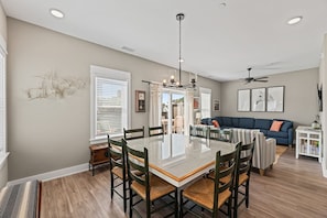 A dining area with a glass-top table and chairs, a ceiling fan, and a sofa in the background.
