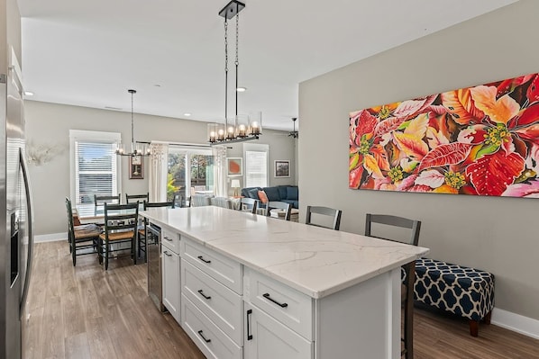 A modern kitchen with a large island, pendant lighting, and a vibrant floral painting on the wall.