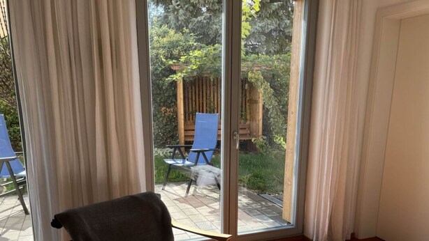 Quarto com uma grande porta de correr de vidro que dá para área externa com deck de madeira, uma cadeira azul e uma mesa pequena.