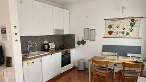Cozinha compacta com armários brancos, bancada de madeira e área de refeições com mesa e cadeiras.