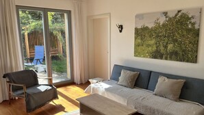 Uma sala de estar com um sofá, uma poltrona, uma mesa de centro e uma porta de vidro deslizante que dá para uma área externa com uma cadeira e uma mesa.