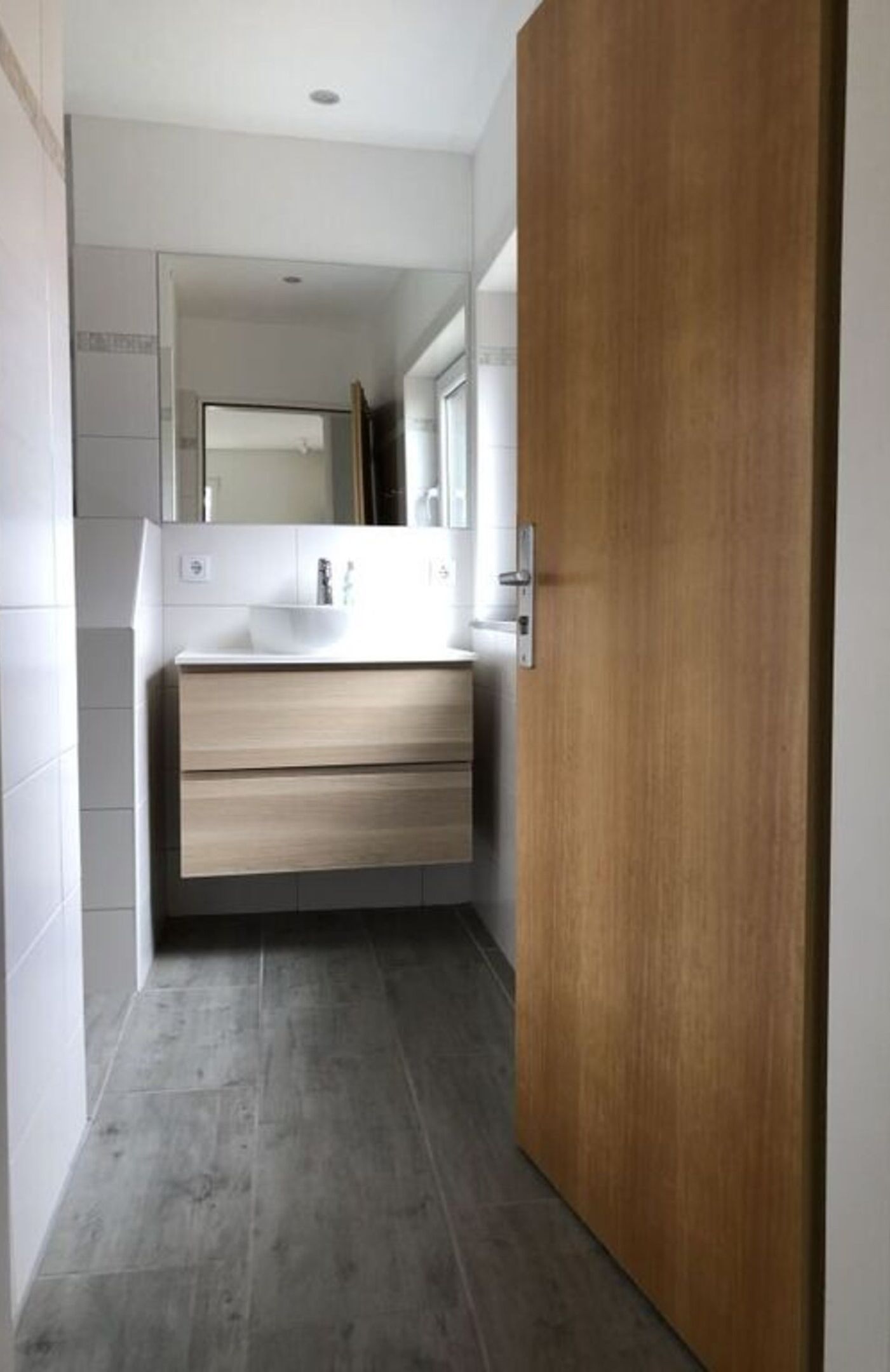 A modern bathroom with a wooden door, a white sink, and a mirror above it.