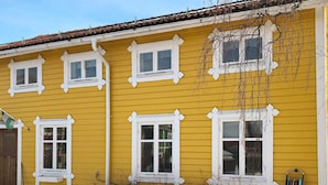 Un bâtiment jaune avec des bordures blanches, de nombreuses fenêtres et un enrouleur de tuyau visible sur le côté.