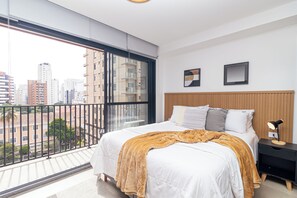 Ein modernes Schlafzimmer mit großem Fenster, einem Bett mit weißer und goldener Decke, einem Holz-Kopfteil und einem Nachttisch mit Lampe.