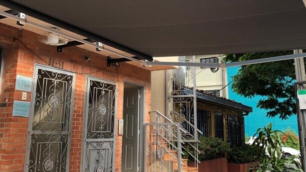 Un edificio con ingresso coperto, cancelli in metallo e una scala che conduce a un secondo piano.