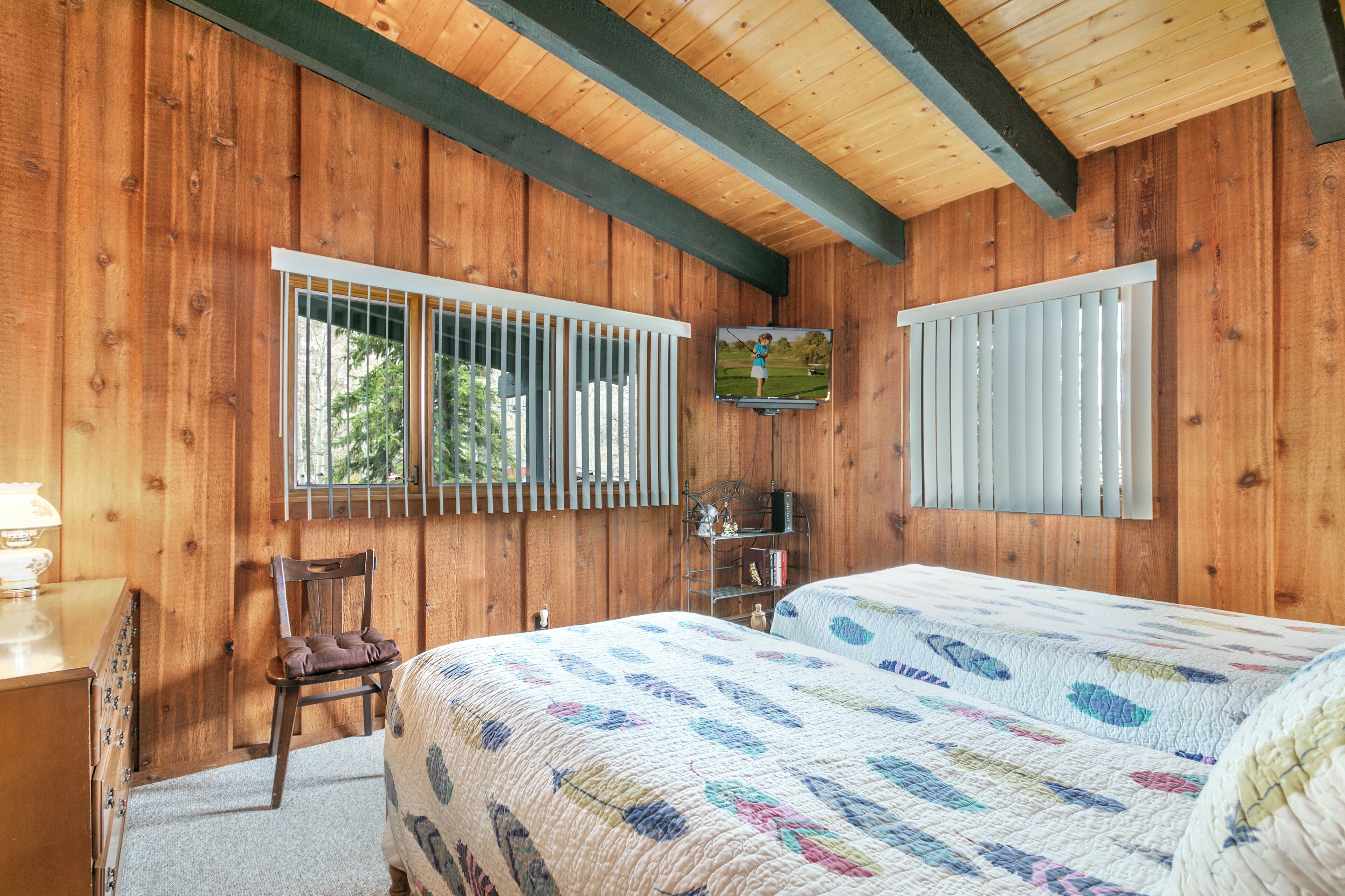 Een slaapkamer in een houten chalet met een bed, een stoel, een televisie en een raam met luxaflex.