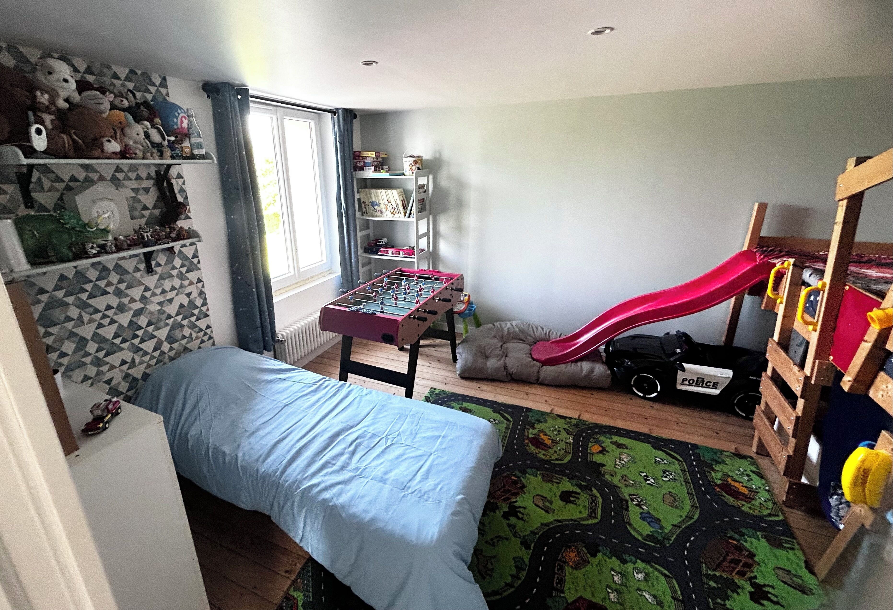 Habitació infantil amb un llit, una zona de jocs amb tobogan i una taula de futbolí.