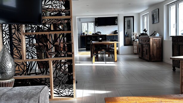 Un salón amplio con una mesa de centro de madera, un sofá gris y un panel decorativo en la pared.