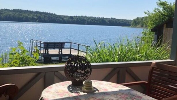 A covered outdoor seating area with a table and chairs, overlooking a lake. - Schaalseehobbit Modern Retreat (Seedorf)