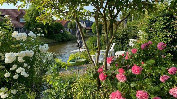A garden with white and pink flowers, a fountain, and a river in the background. - Cosy Holiday Home Near the Centre (Krummhoern)