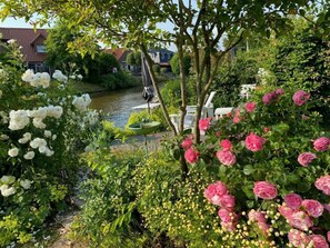 Un jardin agrémenté de fleurs blanches et roses, une fontaine et une rivière en arrière-plan.