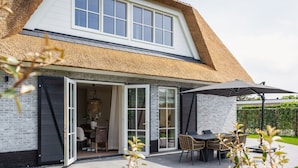 A modern house with a large open patio, a dining area with outdoor furniture, and a thatched roof.