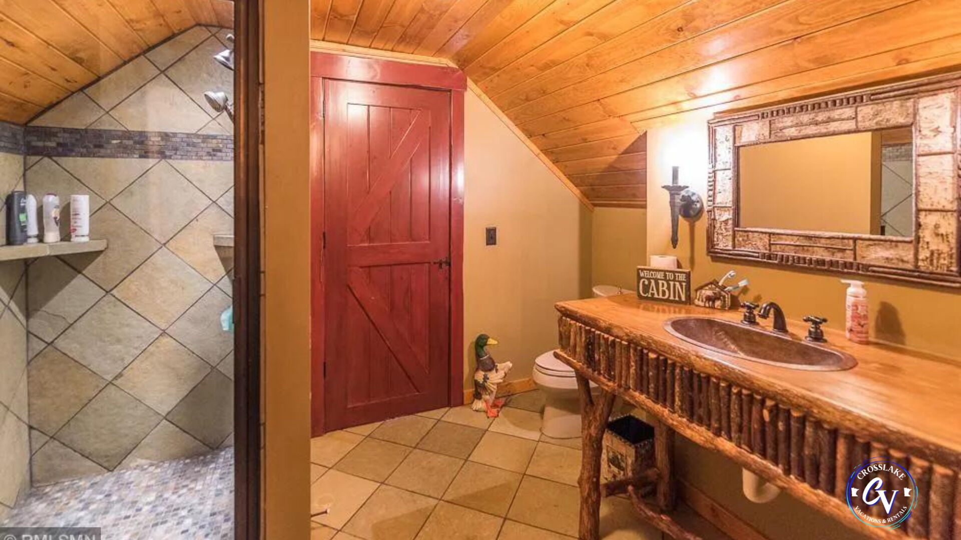Une salle de bain avec un meuble-lavabo en bois, un grand miroir et une porte rouge.