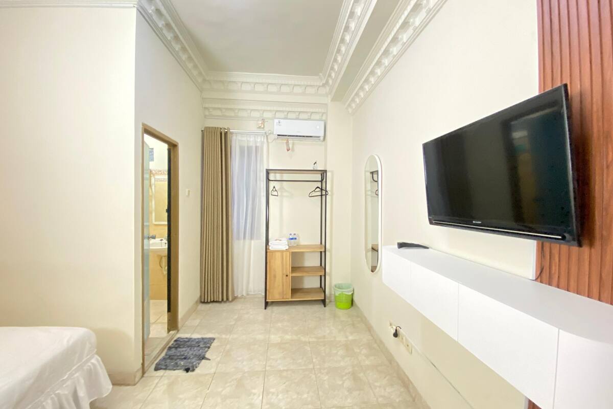 Habitación de hotel con cama, televisión montada en la pared, armario, espejo y zona de ducha.
