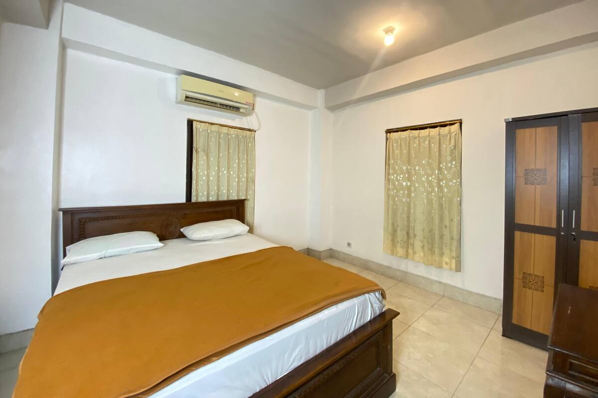 Un dormitorio con cama, aire acondicionado, armario y ventana con cortinas.
